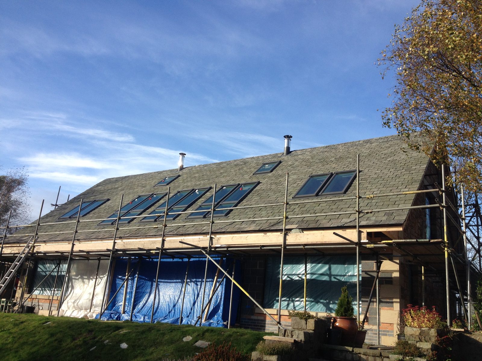 Steep grey tiled roof with a run of roof windows, metal flues and scaffolding