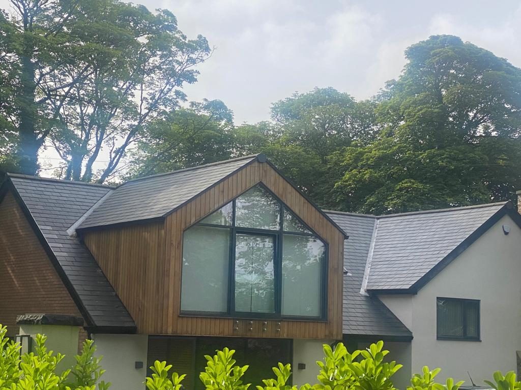 Finished dark slate roof on a cream house with a timber-clad gable and valley flashing