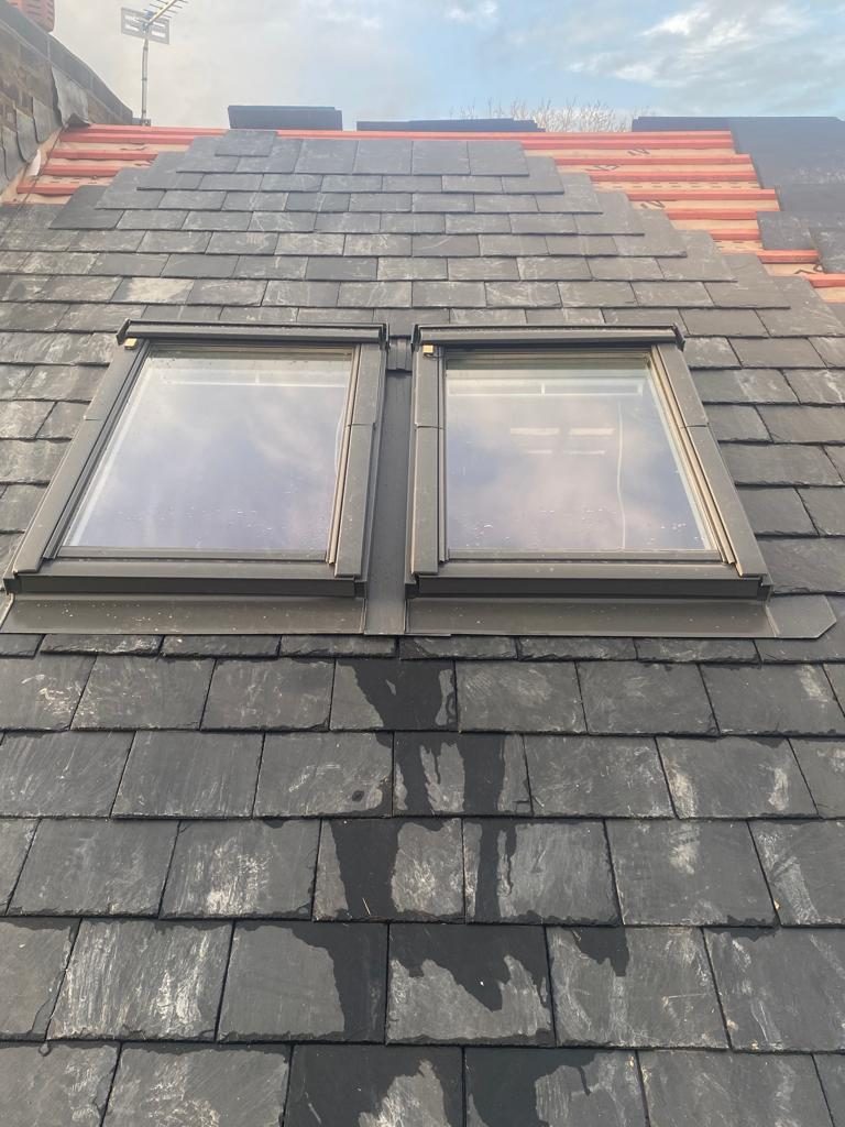 Dark slate roof with two roof windows and battens still open at the ridge